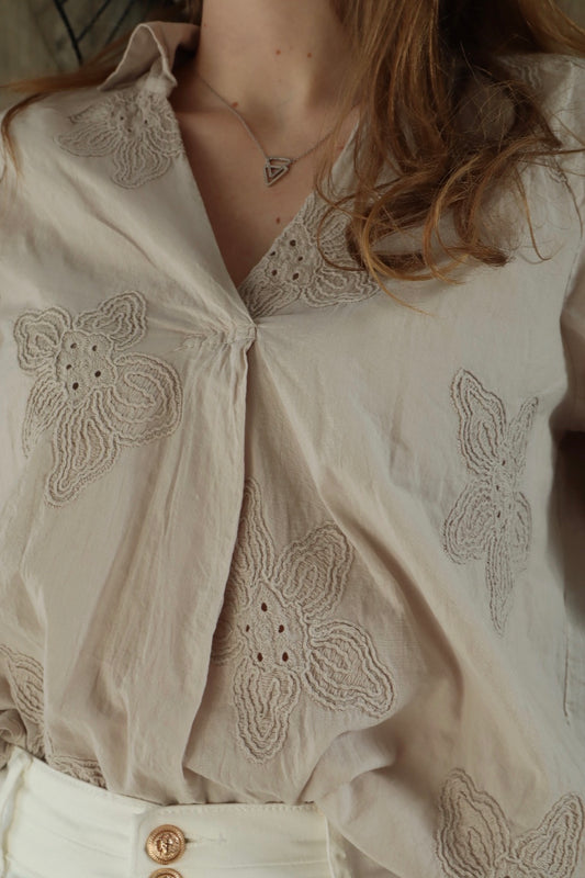 Féminité délicate : Plongez dans le charme discret de cette blouse beige, où les motifs floraux en relief évoquent la fragilité et la beauté de la nature, pour une allure romantique et élégante.